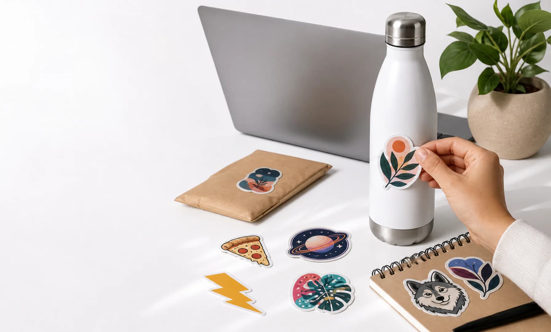Bright workbench with a laptop, bottle, mailer, and original colorful vinyl stickers